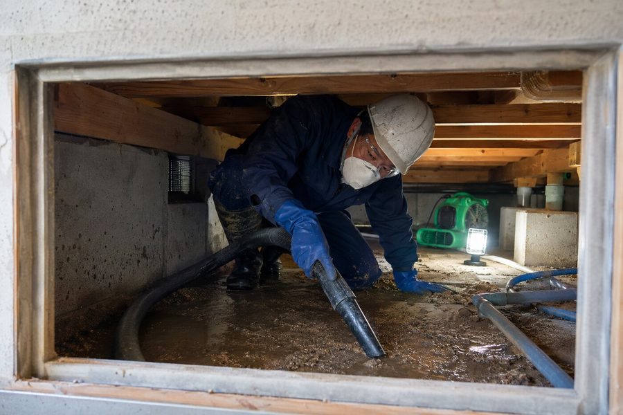 床下に残った水と汚泥を吸引除去する水害復旧作業員